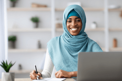 Black professional Muslim woman with a blue head scarf and smiling face.