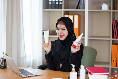 Smiling Young Businesswoman Wearing Hijab While Working In Office and Holding Beauty Products.