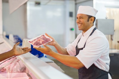 Happy butcher handing meat to customer.