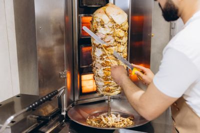 Chef slicing shawarma from vertical grill.