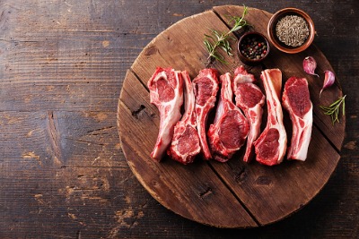 Raw fresh lamb ribs with pepper and cumin on wooden cutting board on dark background.