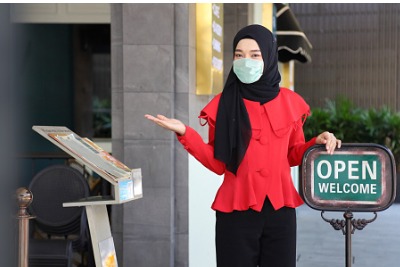 Muslim lady greeting customers wearing face mask.